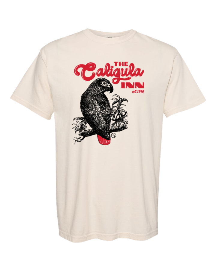 A cream colored tee shirt. On it is an illustration of an African Grey parrot with a blood red tail. Text above reads "The Caligula Inn est. 1996"