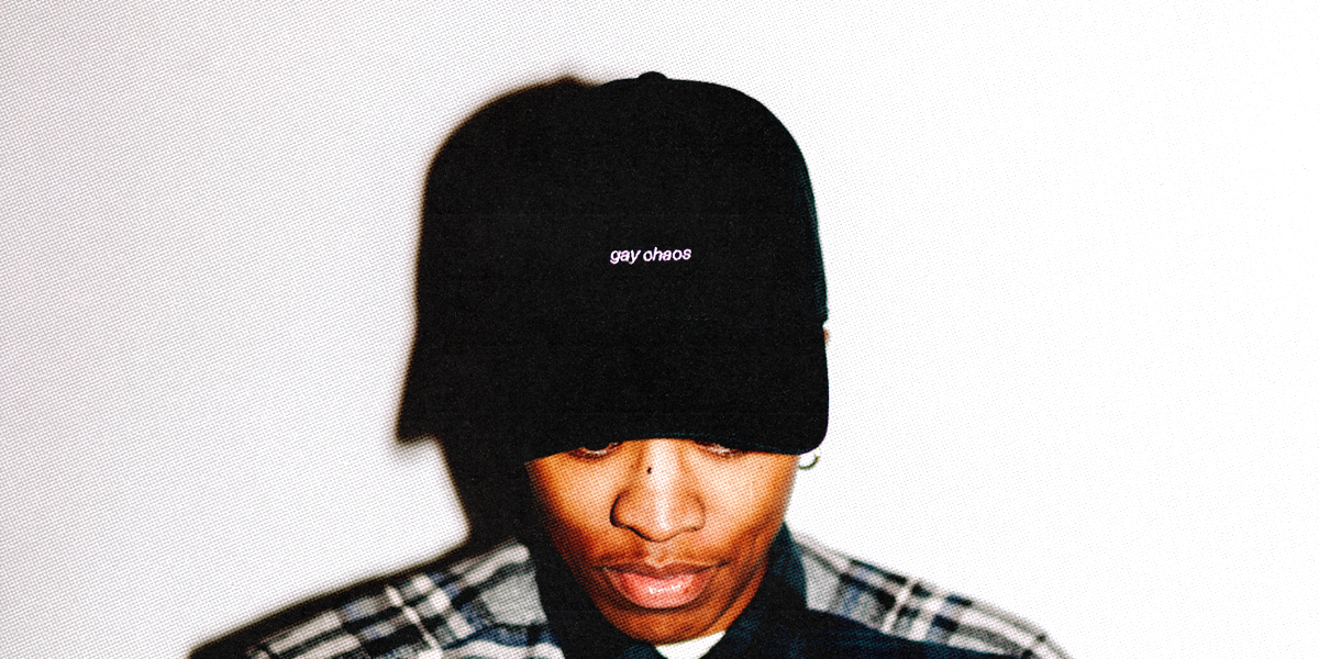 a black hat that says gay chaos in small lettering on the head of a queer person who is looking down